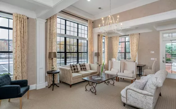 Elegant lounge with a long sofa, armchairs, coffee table, and large windows with patterned curtains. Chandelier overhead.