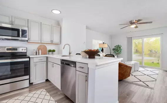 Modern kitchen with white cabinets, stainless steel appliances, island, and open view to a living room with a sliding door.