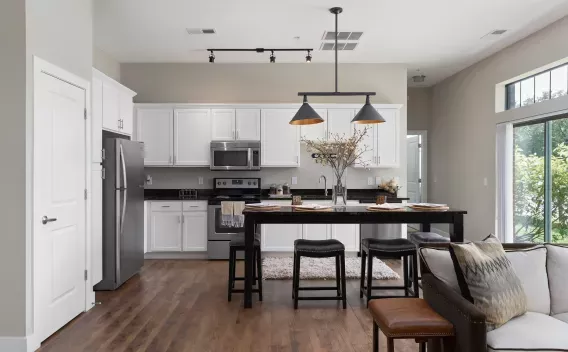 Bright, open-concept kitchen and living space with white cabinets, dark counters, stainless appliances, and a large island.
