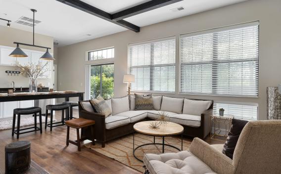 Modern open-plan living room with L-shaped sofa, coffee table, and view into kitchen with island. Hardwood floors.