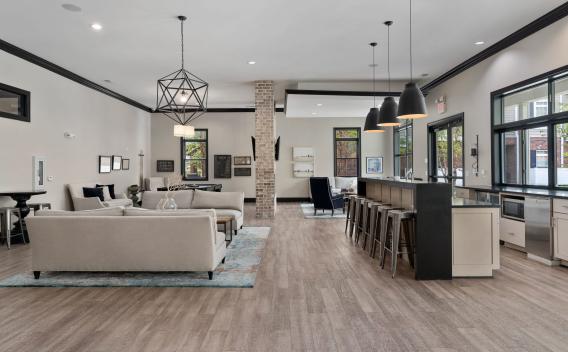 Modern lounge with light sofas, geometric pendant lights, a bar with stools, and a small kitchen area.