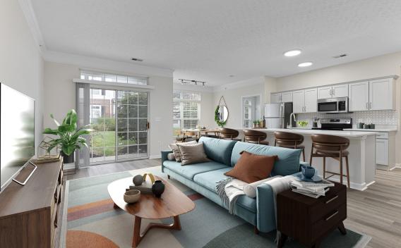 Modern living room with blue sofa, colorful rug, and patio, open to dining area and white kitchen with island bar.