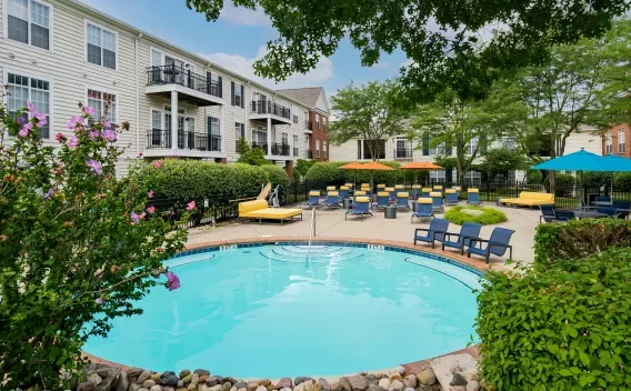 Apartment complex pool with blue water, yellow lounge chairs, blue umbrellas, and a building with balconies.