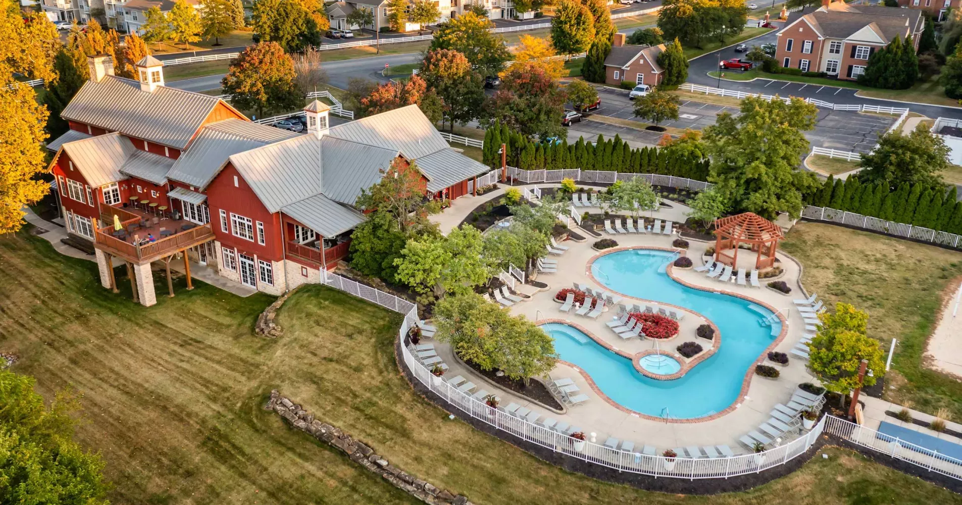 Aerial photograph: Red clubhouse with a large swimming pool, surrounded by autumn trees and a residential neighborhood.