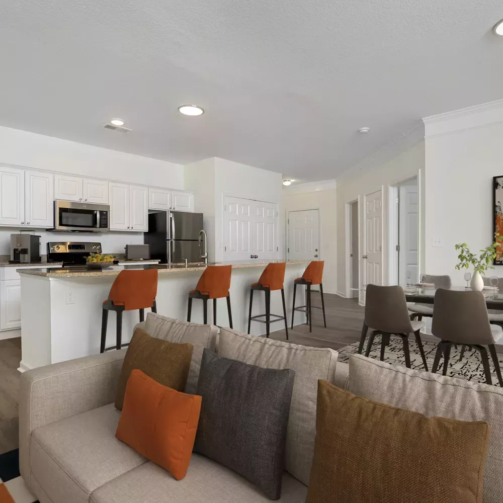 Open-concept living room, kitchen with orange bar stools, and dining area with abstract art.