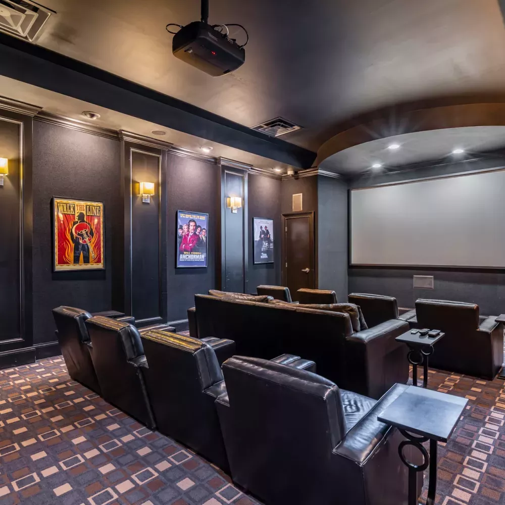 Dark home theater with projector, large screen, rows of leather recliners, and movie posters.