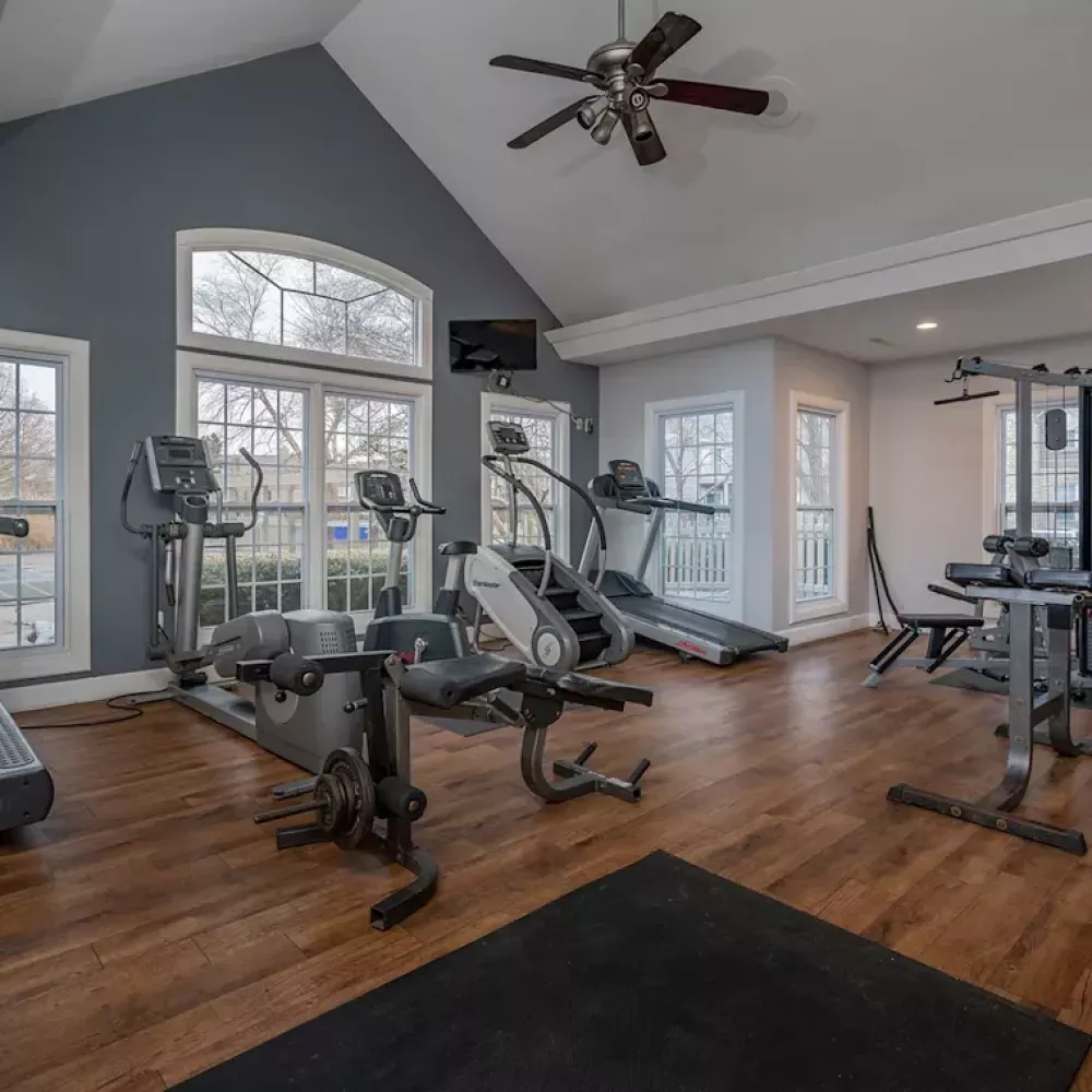 A well-equipped gym with treadmills, ellipticals, weight machines, and a dark gray accent wall under a vaulted ceiling.