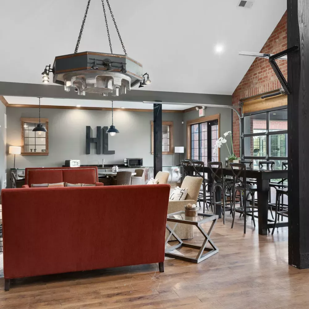 Modern common room with a red sofa, stone fireplace, exposed brick, high-top tables, and a large "HIL" sign.
