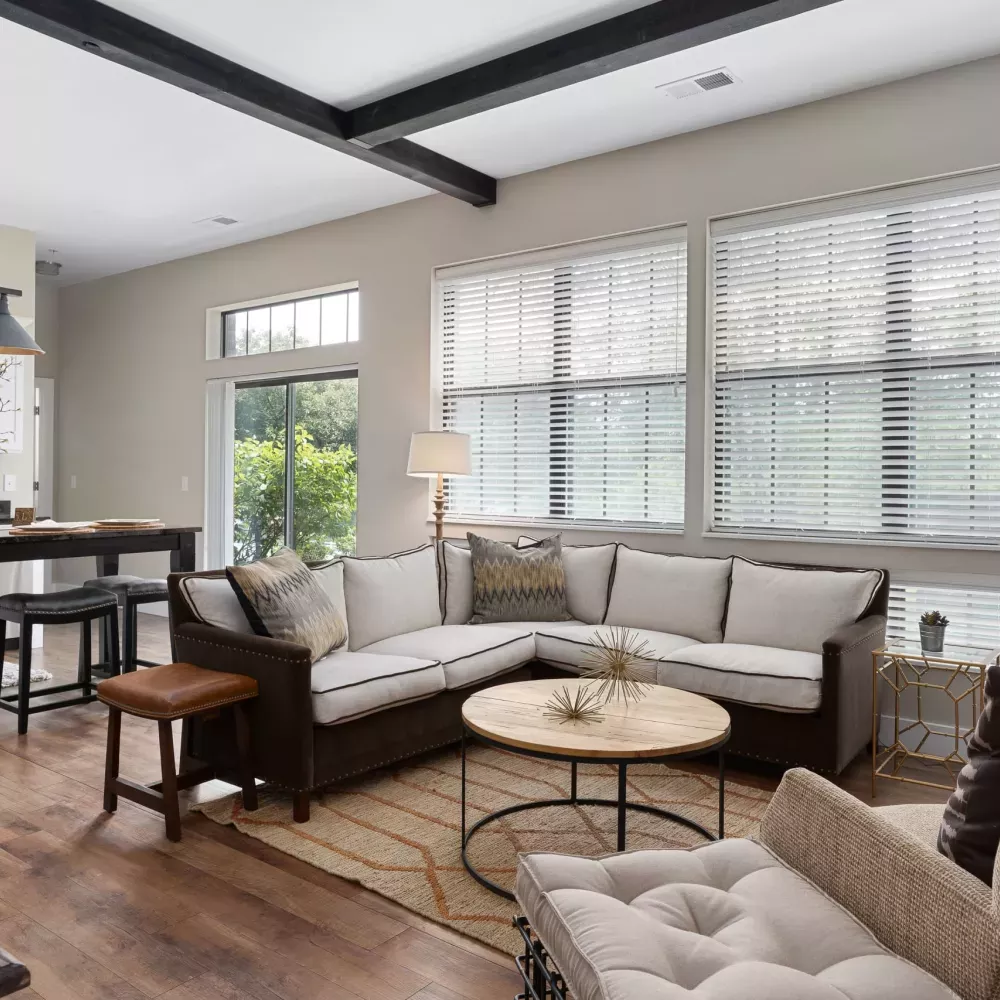 Modern open-plan living room with L-shaped sofa, coffee table, and view into kitchen with island. Hardwood floors.