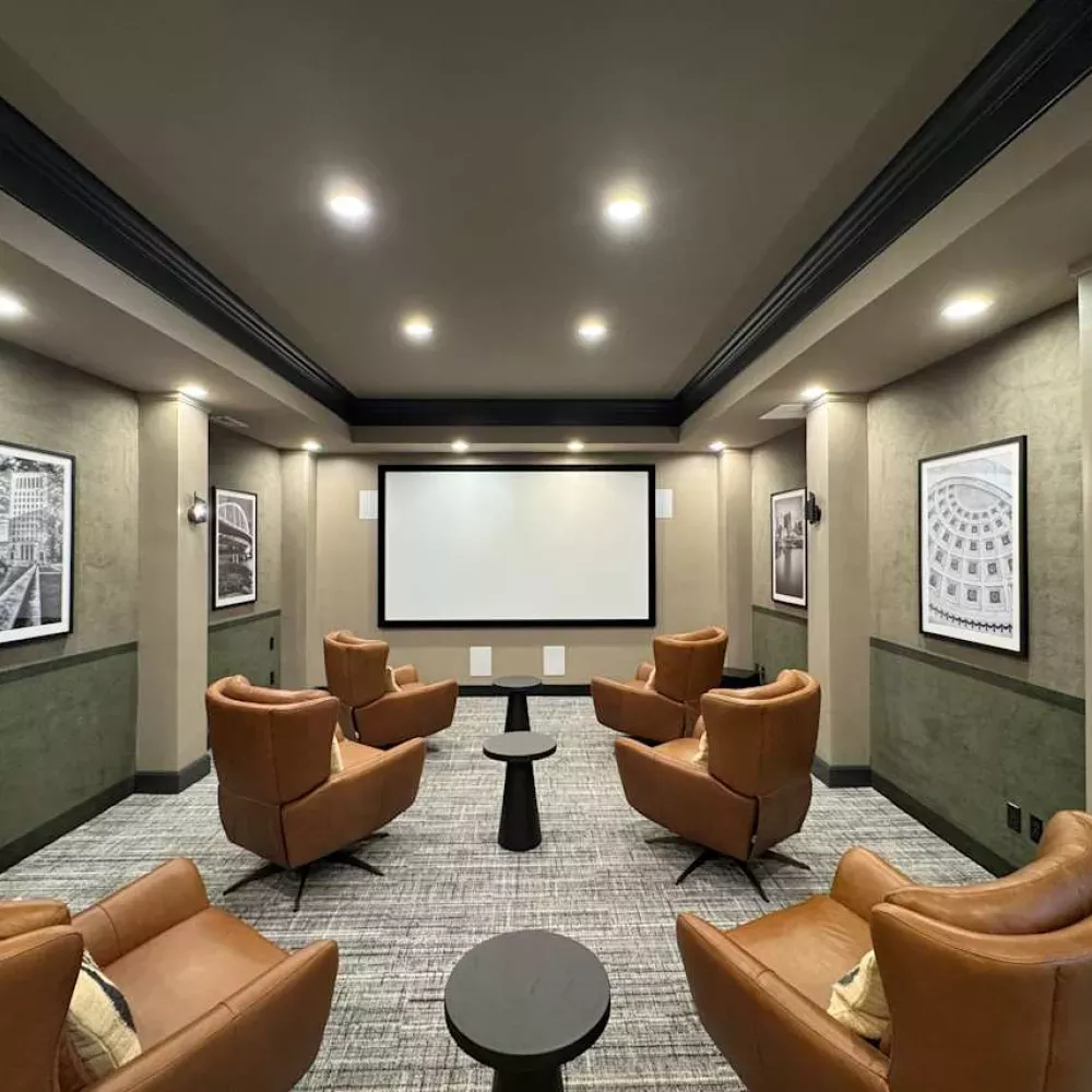 Stylish private screening room with six brown leather chairs facing a large projection screen and framed artwork.
