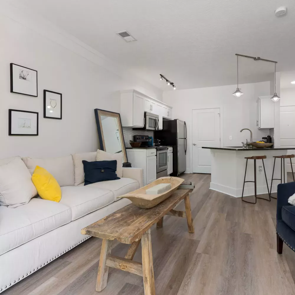 Modern open-concept living room and kitchen with a cream sofa, blue armchair, and rustic wood coffee table.