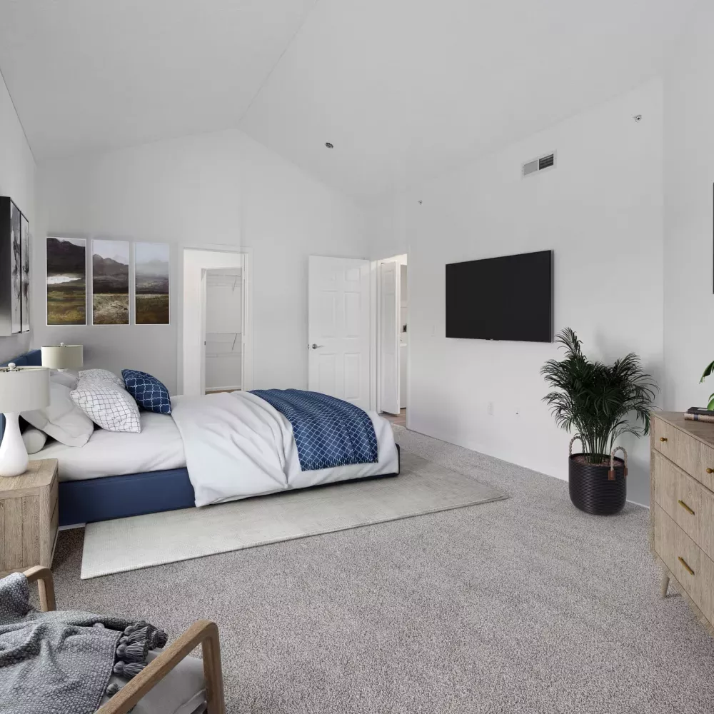 Bright bedroom with vaulted ceiling, bed with blue and white bedding, wall-mounted TV, wooden dresser, and highland cow art.